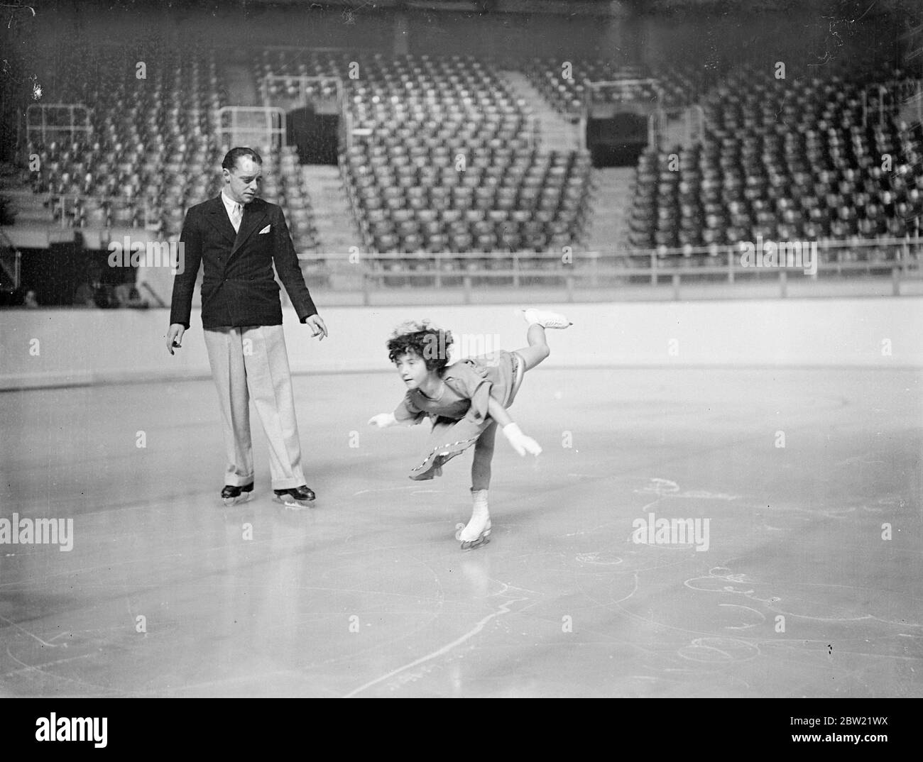 Five-year-old Beryl Bailey practices on the ice at Harringay Stadium, London under the critical eye of Albert Potts. Beryl gave an exhibition when the new season opened at the stadium, experts believe that in a few years she will be a champion. 19 September 1937. Stock Photo
