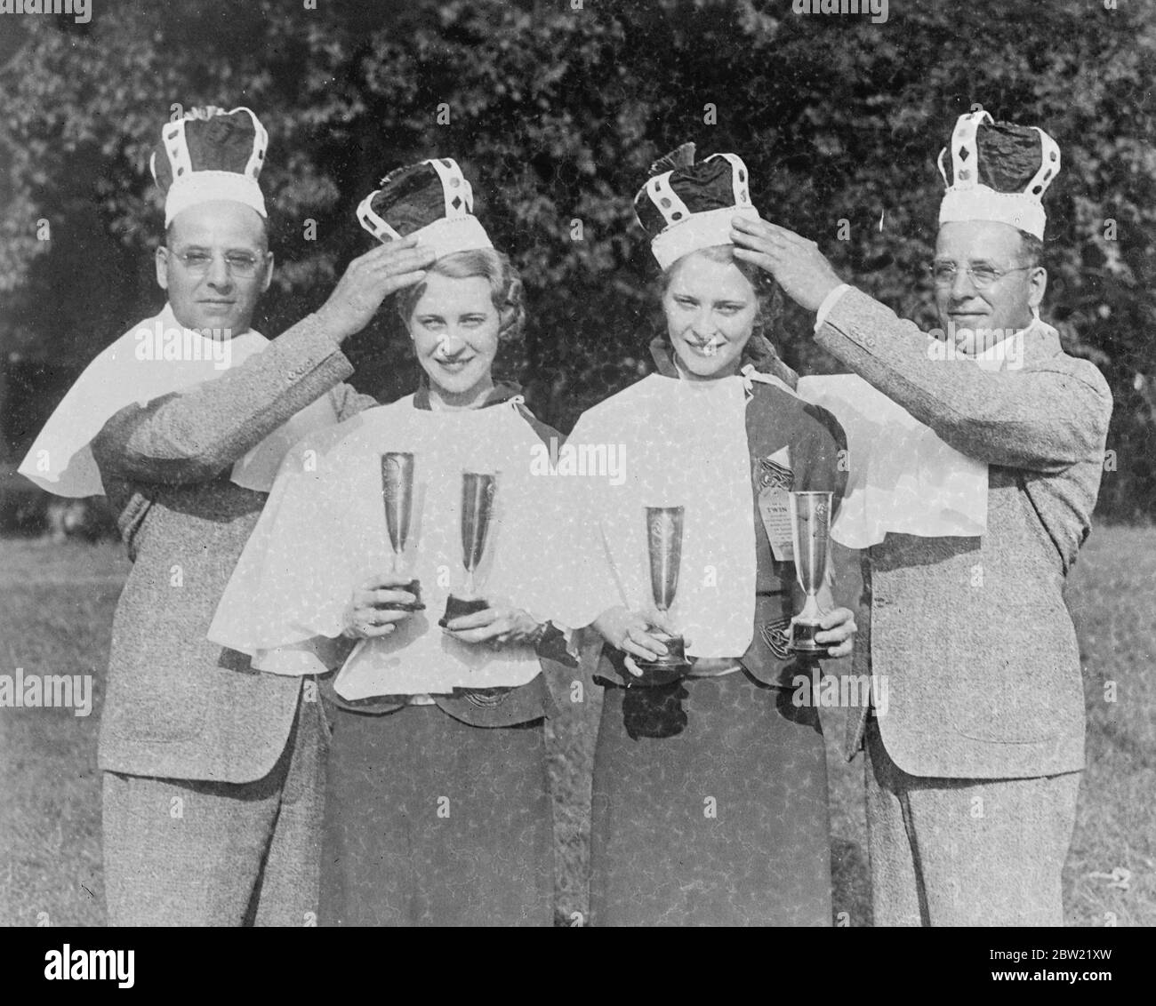 Homer Klopfenstein (left) and his twin brother, Howard, crowning Alta (left) and alva Dank at the National Twins convention, Fort Wayne, Indiana, US. The 25-year-old twins were the best match winning at the National tent convention. The couple's reigned as co-Kings and co-cqueens which was attended by more than 2500. 8 September 1937. Stock Photo