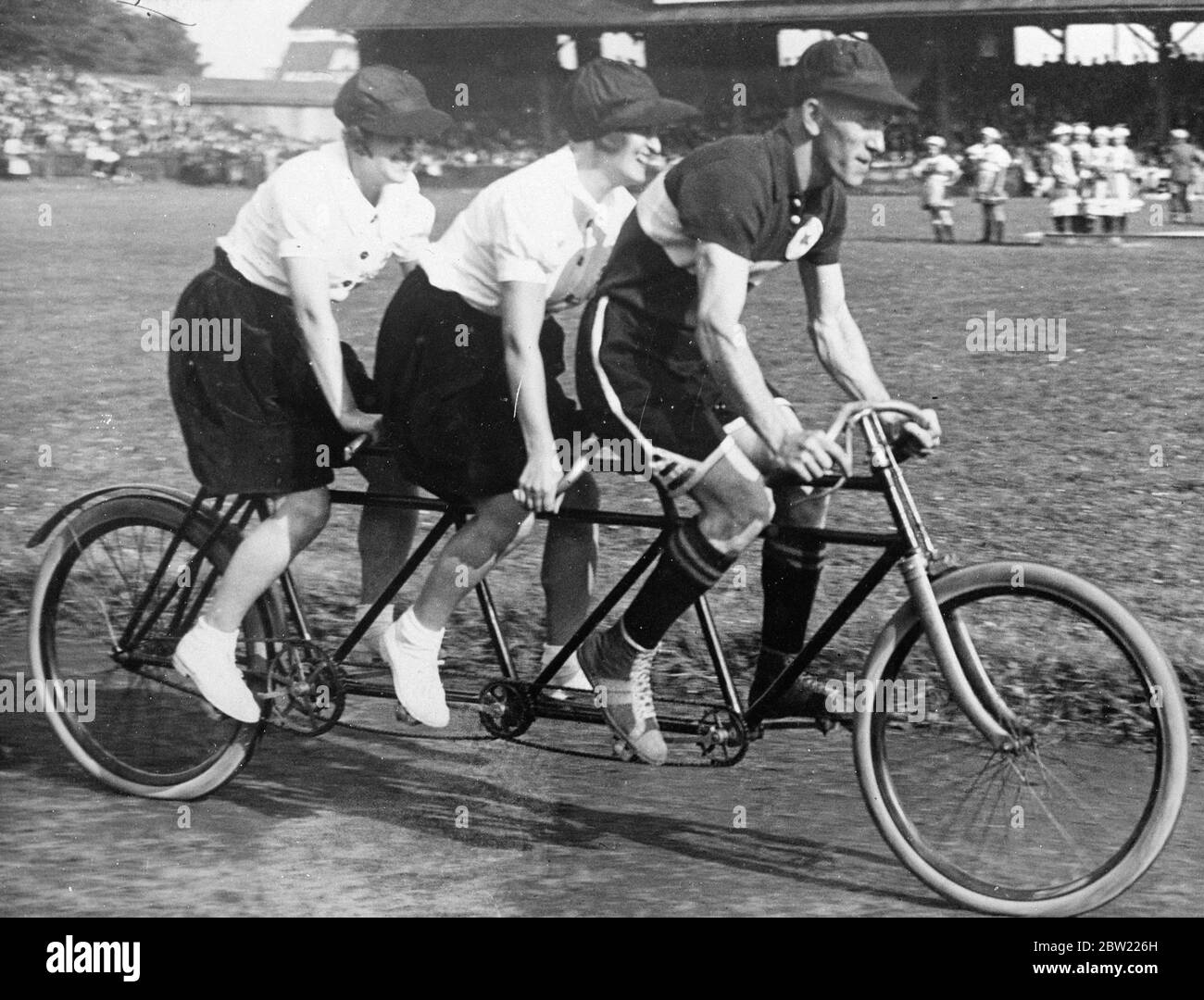 the old adage that twos company, three's a crowd being disproved by an Austrian cycle manufacturer who has produced a machine-an improvement on the tandem-made for three people. Picture shows the three seater cycle at a Vienna meeting. 30 September 1937. Stock Photo
