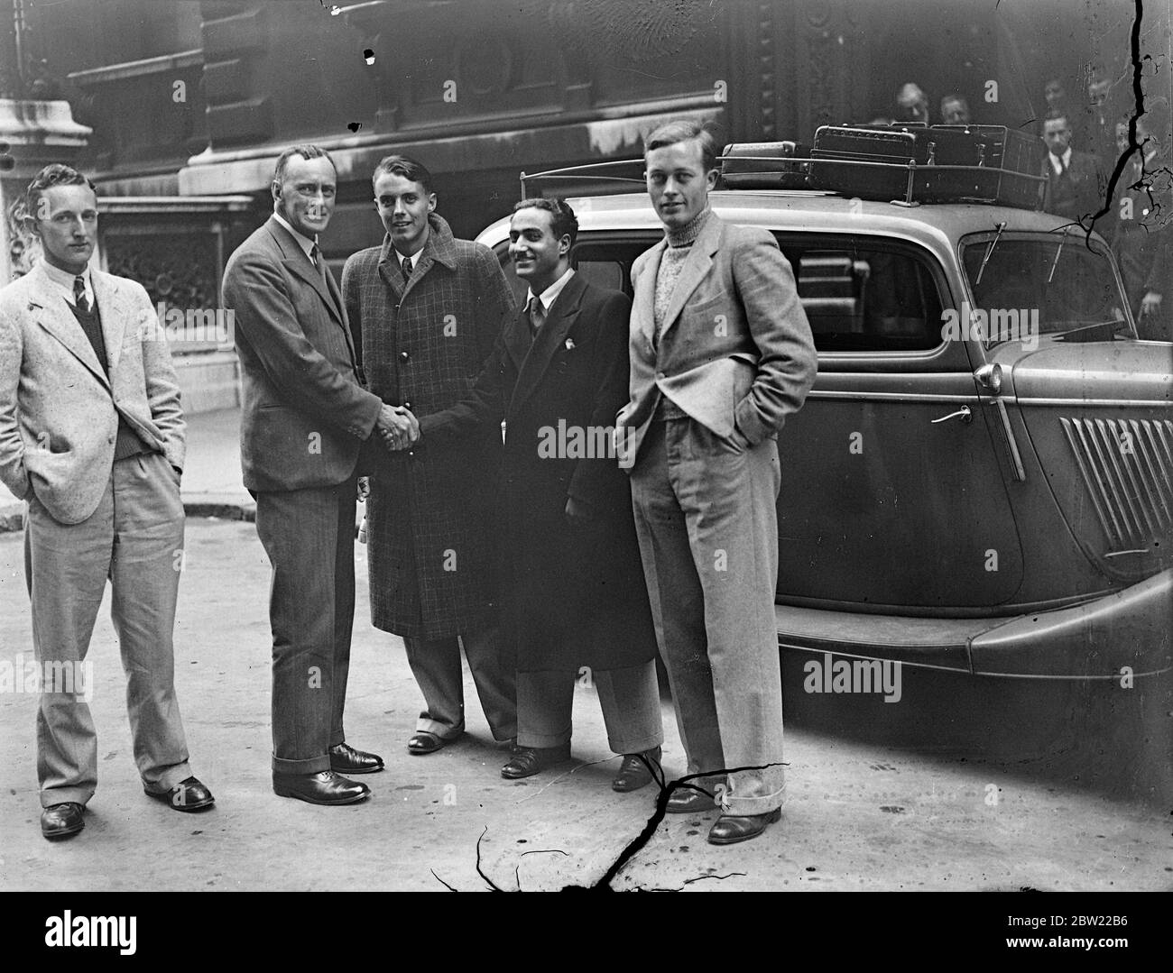 Four English boys began their new career in adventurous style when they left the India Office in London to travel by car all the way to Calcutta take up positions in the Indian Civil Service. S. K. Brown (second from left) Assistant Under-Secretary for India shaking hands with the boys as they left London (left to right): A W Flack, T. N. Kaul, F. A. Sharpe and P. F. Adams loading their car with petrol before leaving London. 21 September 1937. Stock Photo