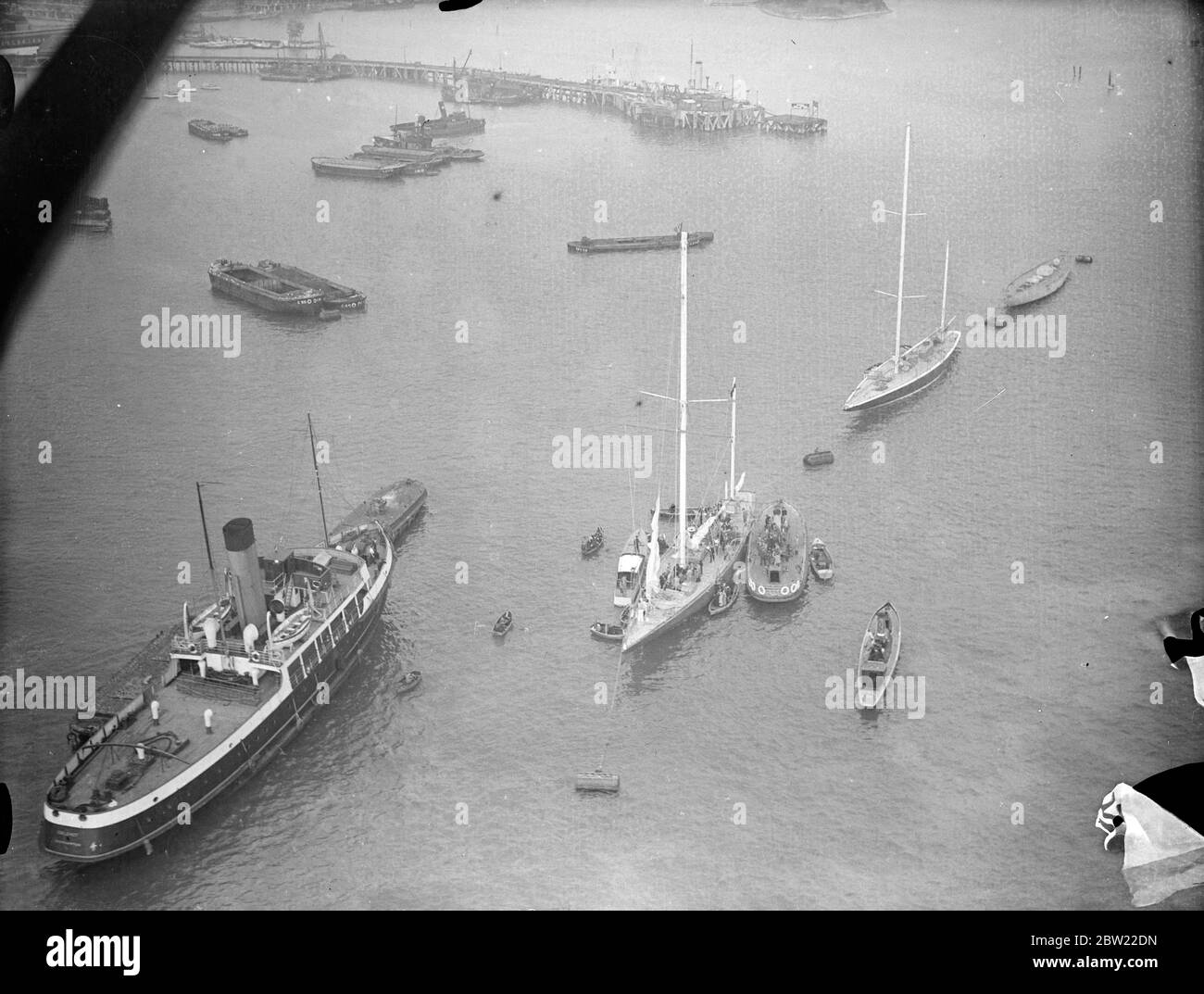 A view from the air as other craft flocked around the yacht to welcome her on her arrival. Captain Nad Heard, master of the endeavour I, after bringing their yachts safely into port in Hampshire. After their lone 2000 mile voyage across the Atlantic. 1 October 1937. Stock Photo