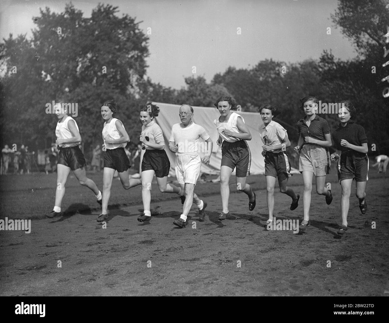 Age trains youth in Battersea Park. Veteran member of the Belgrave Harriers, 57-year-old Mr W Fish is training girls of the Spartan ladies Athletic Club in Battersea Park, London. Photo shows, Mr W Fish with goals of the Spartan ladies club in a training run at Battersea Park, London, today (Sunday). 26 September 1937 Stock Photo