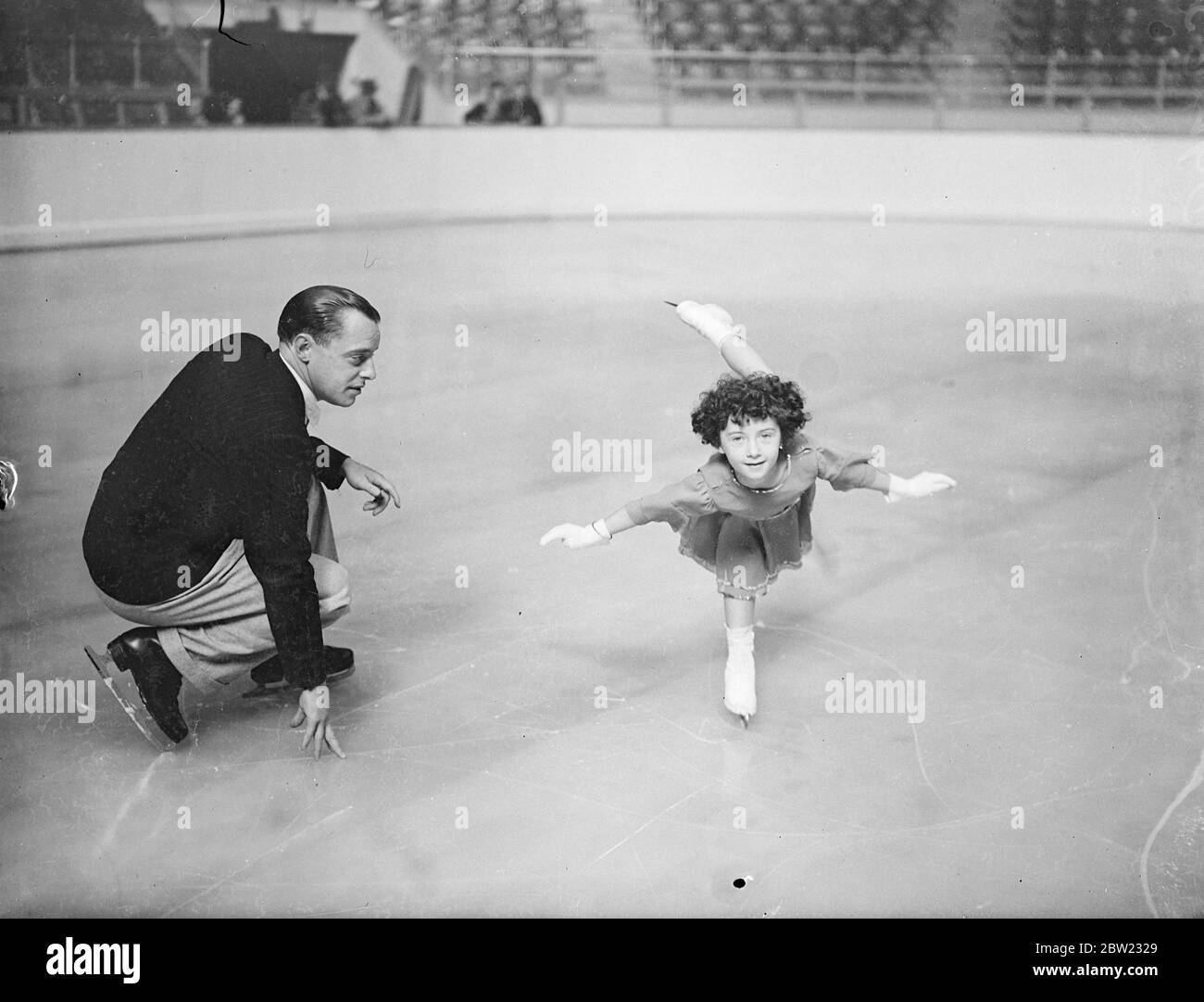 Five-year-old Beryl Bailey practices on the ice at Harringay Stadium, London under the critical eye of Albert Potts. Beryl gave an exhibition when the new season opened at the stadium, experts believe that in a few years she will be a champion. 19 September 1937. Stock Photo