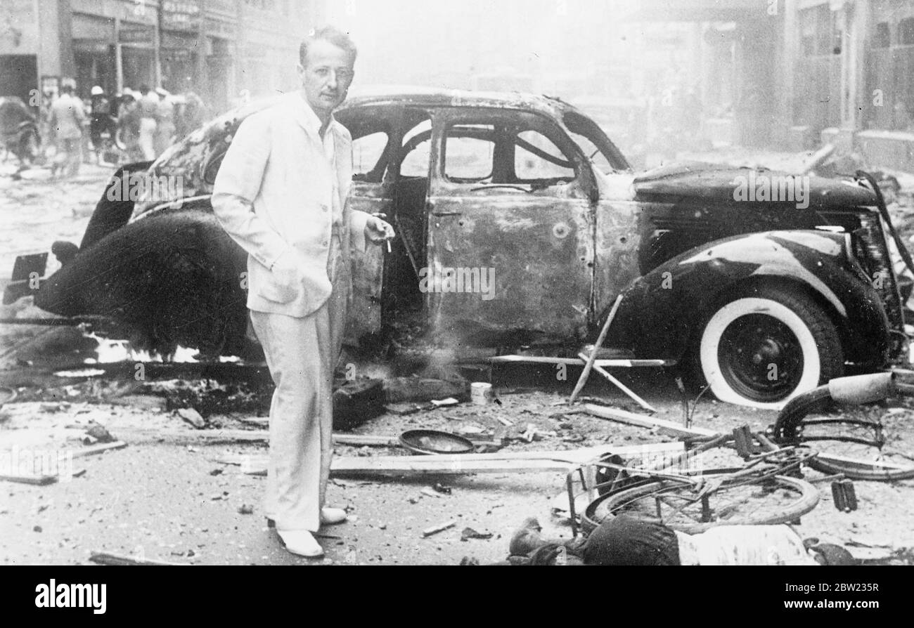 This picture, just received in London from Shanghai, shows John R. Morris, the United Press correspondent, standing beside a wrecked car on the Nanking Road between the Cathay and Palace Hotels, just after several bombs had dropped, killing 140 and injuring 40 people. The bombs were dropped on Nanking Road after planes had attacked the Japanese worship Idzumo. A tremendous crater was left and about 20 cars were completely burnt out. Two foreign motorists were trapped and burned alive. 2 September 1937 Stock Photo