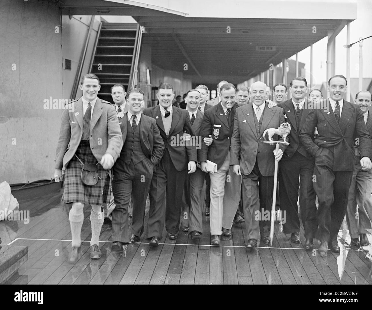 The British rugby team which has been touring South Africa Captained by Sam Walker arrived at Southampton on the Athlone Castle on the return home. The team's tour was highly successful. Out of 24 matches played, 17 were won by the British team, seven being lost. This record is the best of any team that has visited South Africa for 35 years. Photo shows: The British rugby team on their arrival at Southampton. Centre is Major Hartley, the manager, with lion-stick mascot, and on his right is Sam Walker, the captain. 7 October 1938 Stock Photo