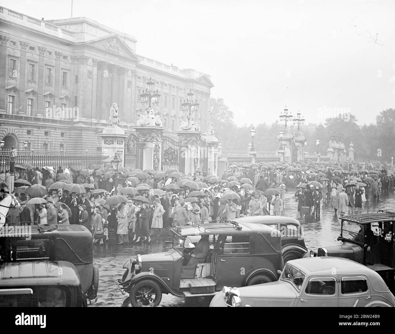 Premiers trial for return to London through cheering crowds. Sees King. Driving through crowds lining the great West Road and other parts of the route, Mr Neville Chamberlain, when from Heston Aerodrome to see the King at Buckingham Palace immediately after landing from Munich, where he has signed a 'No More War' Pact with Herr Hitler. Later he returned to Downing Street where he was welcomed by tremendous crowds. Photo shows, the crowd sheltering under umbrellas as Mr Neville Chamberlain, arrived at the Palace in the rain. 30 September 1938 Stock Photo