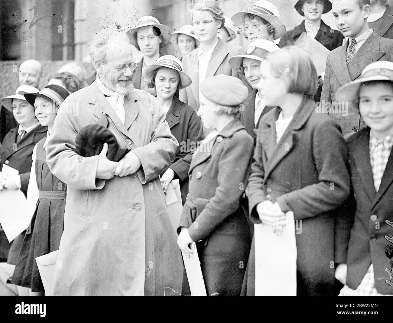 Eric Gill distributes handwriting prizes to London schoolchildren. Mr Eric Gill, the sculptor and engraver, distributed the prizes and certificats awarded as the result of a handwriting competition for schoolchildren sponsored by Mrs John Galsworthy, at County Hall, London. This is the third year in which Mrs Galsworthy has given the sum of Â£90, 5s for prizes in a competition which has for its object the development of a natural handwriting style with 'beauty' legibility and character. Photo shows, Mr Eric Gill chatting with some of the prizewinners after the distribution. 8 July 1938 Stock Photo