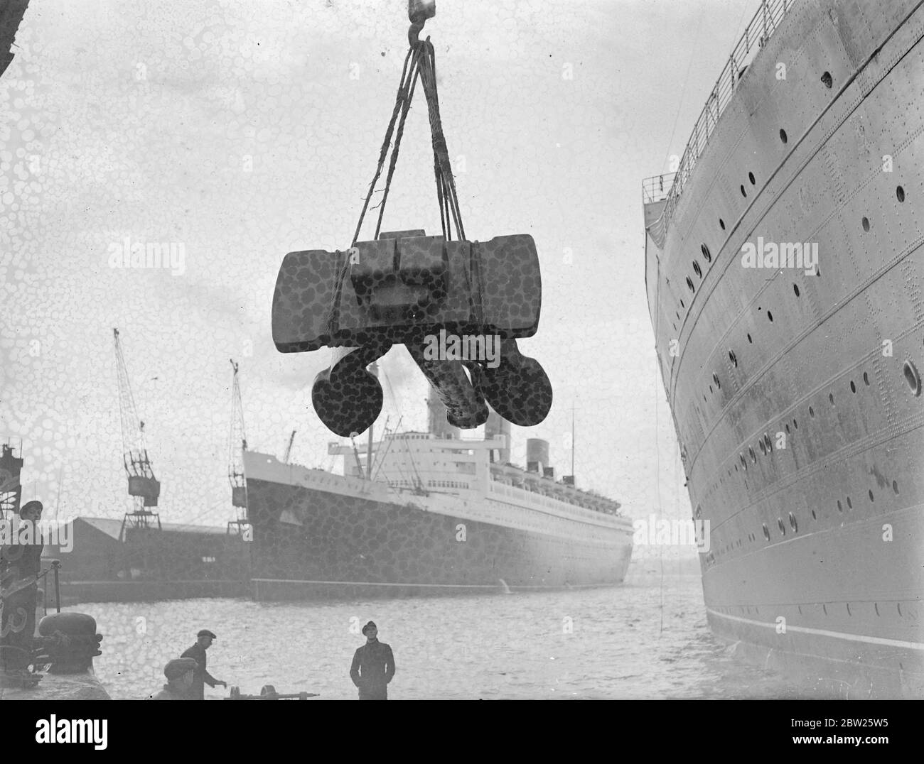 Changing 'Berengaria's' 17 ton anchor at Southampton. The 17 ton bow anchor of the liner 'Berengaria' was changed at Southampton. Immediately on her arrival from New York, in the background is the RMS Queen Mary. 26 January 1938 Stock Photo