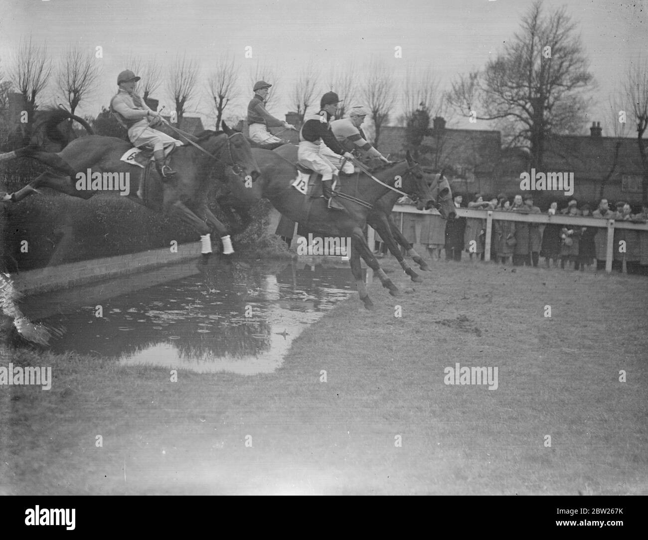 Over the water jump at Sandown. The field taking the water jump in the Park Handicap Steeplechase at the Sandown Park Meeting. No 12 is Pedigree owned by Mr W C Earl and No 6 Merry Abboy II owned by Mr James V. Rank and ridden by Francis. Fort Argos, owned by Wing Commander W R Read won the race. 4 February 1938 Stock Photo