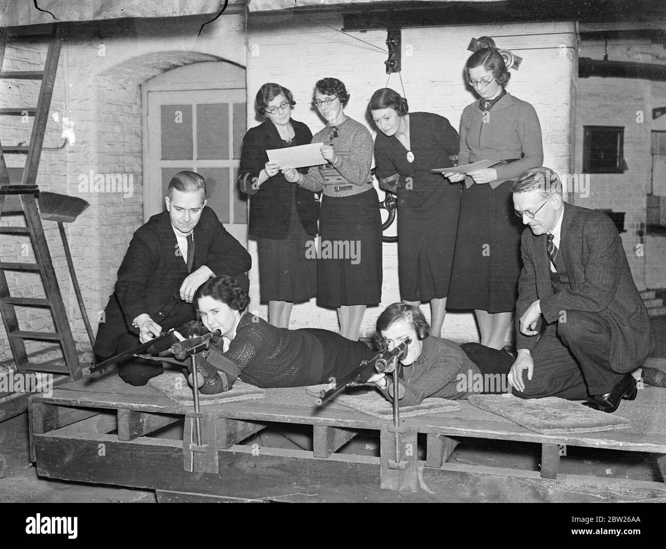 London office girls become expert with the rifle. Girls employed in the offices of the Crown Agents for the Colonies at Millbank, London, have a new interest. They have invaded the shooting range constructed in the basement of the building and spend their lunch hour and much of the time after hours practising marksmanship. They have entered for competitions. Photo shows, two of the girls being instructed by men at the range. 28 January 1938 Stock Photo