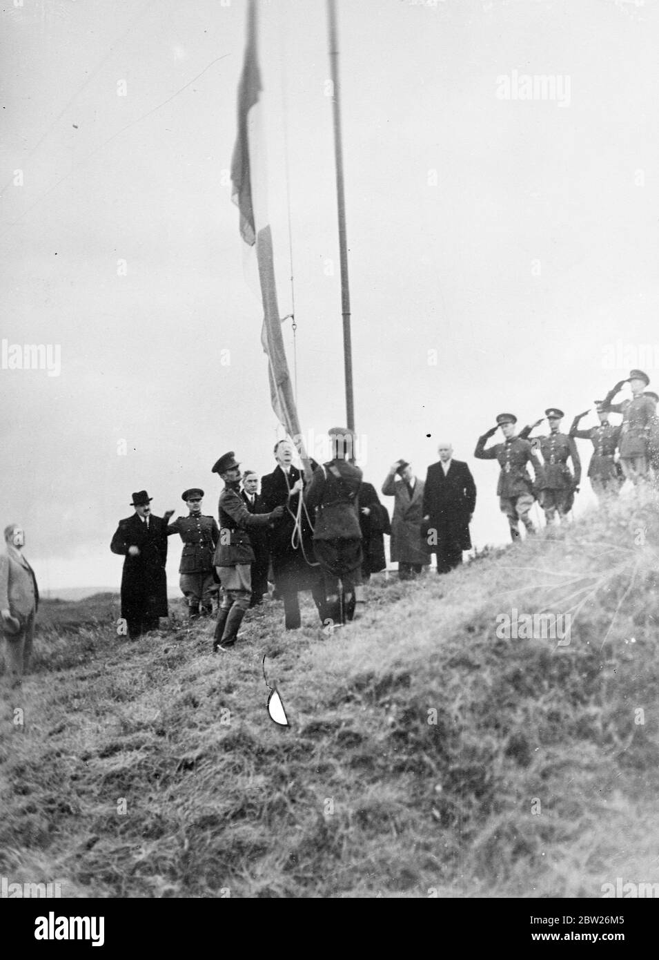 Mr de Valera Hauls up Eire flag at taking over of Spike Island Forts. To the accompaniment of a gun salute, Premier Eamon de Valera hauled up the tricolour flag of Eire on Spike Island, Cork Harbour, to mark the taking over of the forts from the British Army, which has been in command there since 1779 when the island was bought by the British War Office. The forts were handed over under the terms of the recently concluded Anglo Eire agreement. Photo shows, Mr Eamon de Valera hauling up the Eire flag on Spike Island in the presence of dail Mambers. 13 July 1938 Stock Photo