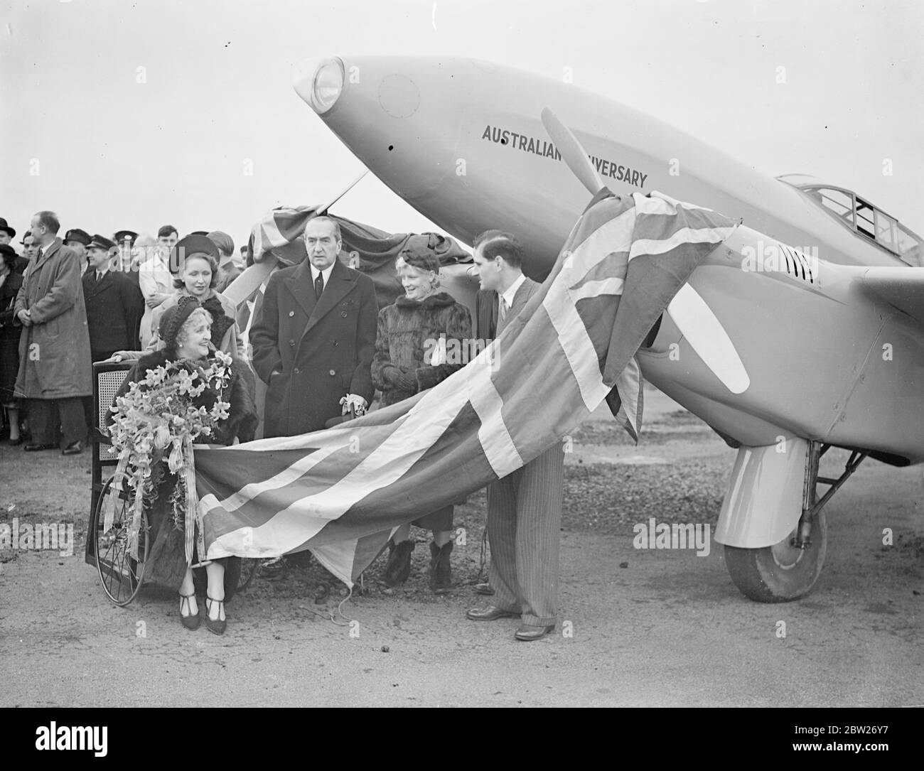 Clouston's ready for New Zealand record attempt, playing christened at Croydon by Lady Weigall from Bath Chair at Croydon. The 220 mile an hour Comet Plane in which flying Ofc, A E. Clouston is to make his New Zealand and back record attempt, was christened at Croydon aerodrome by Lady Weigall, who named it 'Australian Anniversary'. Mr SM Bruce, the Australian High Commissioner, was present at the ceremony. Clouston hopes to accomplish the record journey in nine days. The flight is to start next Monday. Photo shows, the scene at the christening, Lady Weigall in her bath chair. 3 February 1938 Stock Photo