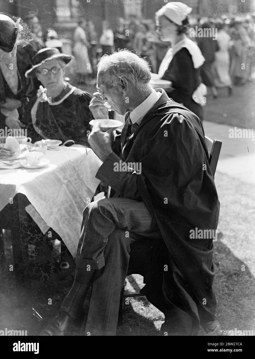 Sir Alan Mawer, the Provost, in his robes, eats an ice on the lawn. Students and the academic staff took tea on the lawns of the College after the presentation in the Great Hall at the Annual Assembly of Faculties of University College, Gower Street. 1 July 1937 Stock Photo