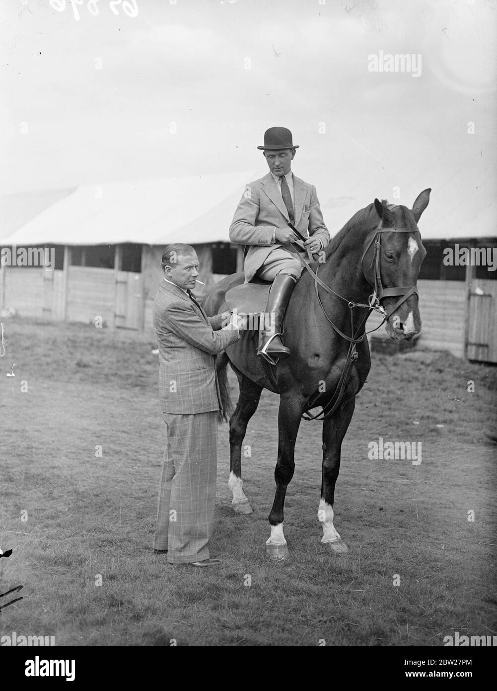 Jack Payne completes at Hatfield show. Jack Payne, the dance band leader, entered his horse 'Odd Socks'in the open jumping at the Hertfordshire Agricultural Show, held in Hatfield Park, Hertfordshire. Photo shows, Jack Payne, tightening the girth of his entry 'Odd Socks'which is ridden by Tom Masson 23 June 1937 Stock Photo