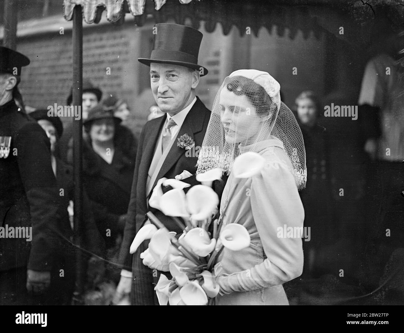Turf wedding in London, director weds his woman chief. The bride, Miss Constance Dagnall, hid her face with her, bouquet when she left St Mary's Church, Cadogan Street, after her marriage to Maj George Anne. Major Anne is managing director of Tote Investors, Ltd, and is well known in racing circles. Miss Dagnell is chief of his telephone staff. Photo shows, the bride and groom leaving. 22 Janary 1938 Stock Photo