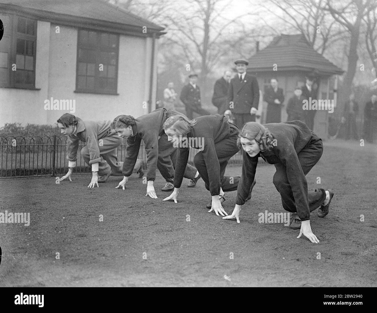 'Starting' to keep warm-girl athletes defy gloomy Sunday whether in London. Despite cold and mist, hardy girl members of the Victoria Park Ladies Athletic Club had the Sunday practice in Victoria Park. Photo shows, members of the Victoria Park Ladies Athletic Club, wearing long trousers instead of shorts, practising starts in Victoria Park. 28 November 1937 Stock Photo