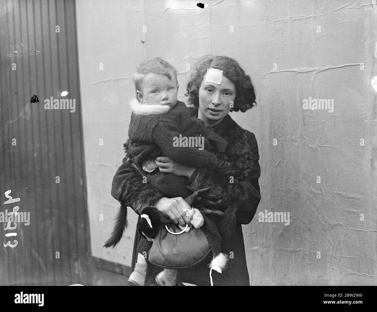 Mothers and babies injured when car mounts pavement in Holloway. Seven taken to hospital. Seven people were injured and taken to hospital when a motor car mounted the pavement in Junction Road, Holloway, London, and crashed into three mothers who were pushing perambulators. Photo shows, Mrs Je Newell (with plaster on head) and her baby, Virginia, who was in one of the parambulators, photographed near the scene after the accident. 30 December 1937 Stock Photo