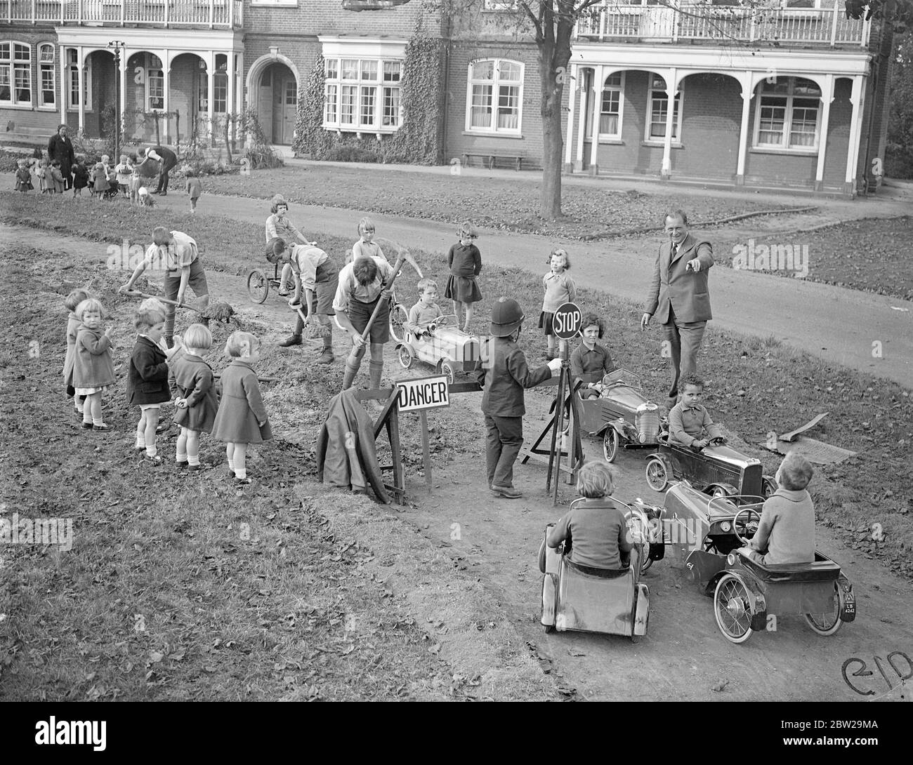 Children taught road sense on their own highway at Essex school. To teach road sent to the 500 pupils at the Hutton (ICC) residential school near Brentwood, Essex, a miniature complete road system with all approved highway signs has been laid out by the pupils in part of the grounds. Children actors 'policeman'while others drive toy motors to and fro. One section of road is permanently 'up'. The scheme is the idea of the headmaster, Mr RC Higdon and he has also instituted and offenders court. Photo shows, one-way traffic-two cars, passing the inevitable roadworks on the miniature highway. 22 O Stock Photo