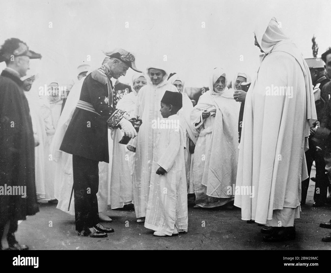 Impressive decoration for a little Prince. General Nogues, representing President LeBrun, in the mist of a gathering of picturesquely robed chieftains, presents the Cross of a French Order to the young son of the Moroccan Sultan during the celebrations commemorating the Sultan's ascension to the throne. 21 November 1937 Stock Photo