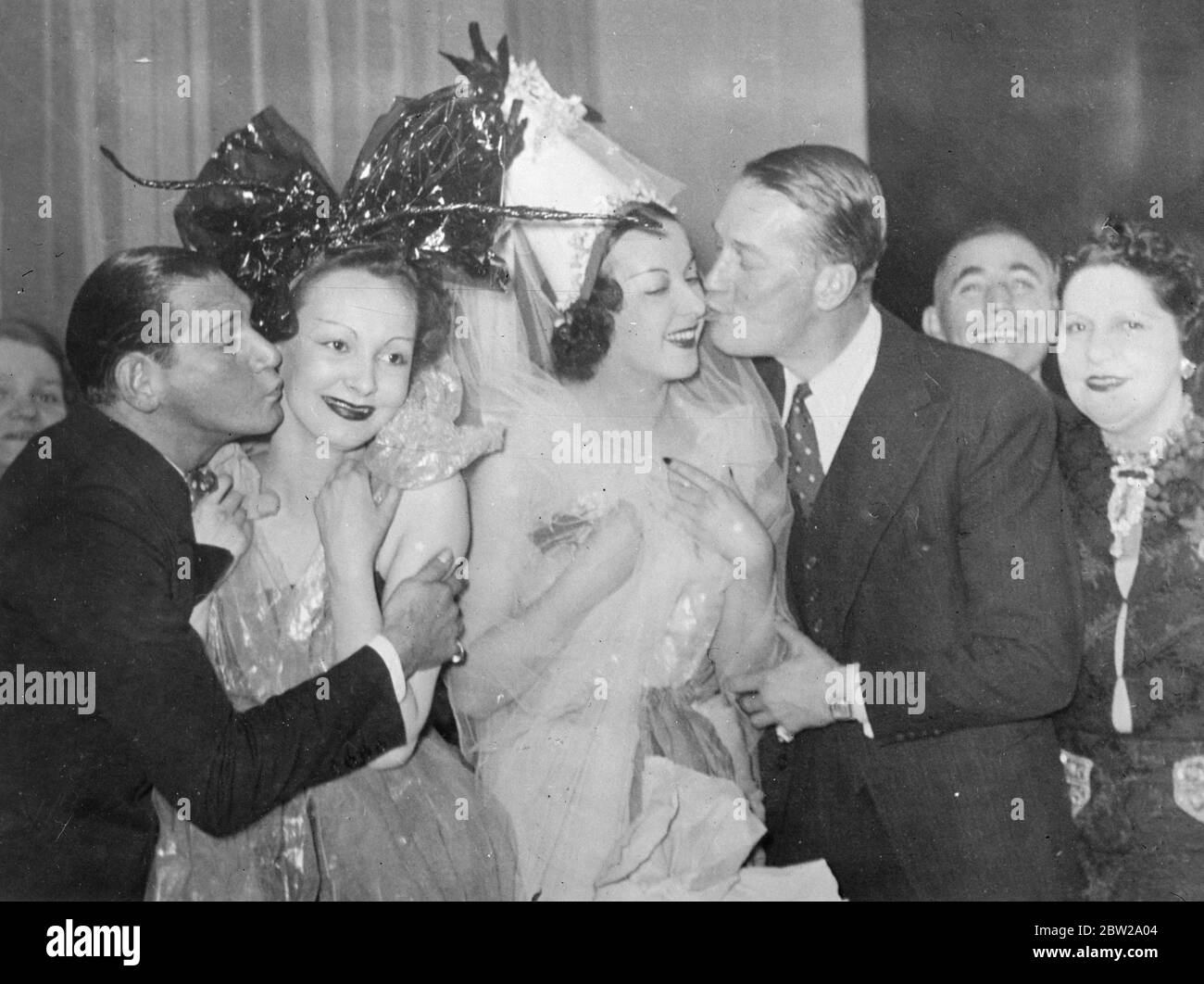 A Chevalier kiss for a Catherinette!. Maurice Chevalier, the film and stage actor (right) and Harry Pilcer, former American dancer and partner of the late Gaby Deslys, stealing kisses from two pretty Catherinettes in Paris during the St Catherine's Day celebrations. Paris 'midinettes' from every dressmaking house in the city, who had reached the aged 25 and were still unmarried, celebrated the Festival of St Catherine, the patron saint, by donning the traditional bonnet and making merry until the small hours of the morning. 26November 1937 Stock Photo