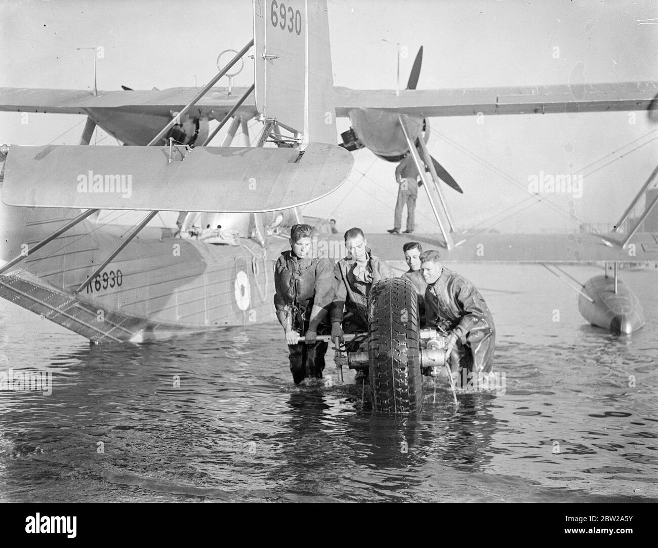 The longest formation flight ever undertaken by service unit, five RAF flying boats of number 204 (Gen reconnaissance) Squadron being prepared at Plymouth. They will take off next week and by the time I return in the Spring, they would have flown 25,000 miles to Australia and back. The visit is being made in connection with the 150th anniversary celebration of Sydney. Photo shows, and bringing ashore one of the drive launching wheels at Plymouth. 26 November 1937 Stock Photo