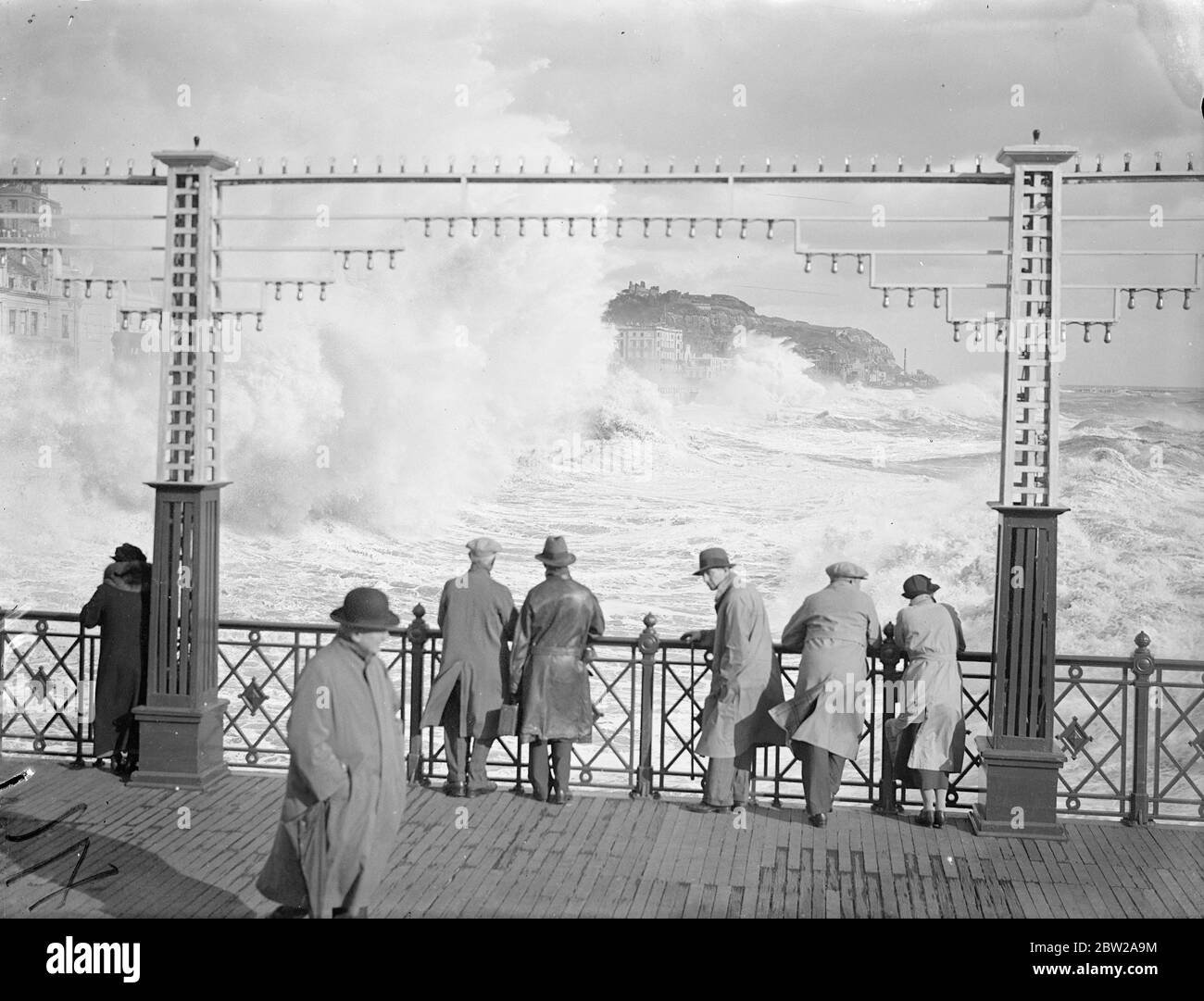 Angry seas spend their forces at Hastings. Angry seas battering in a mist of white spray against the front at Hastings, watched by rain coated men, in the autumn gale which swept the Sussex resort. Gales general over the whole of the south coast. 24 October 1937 Stock Photo