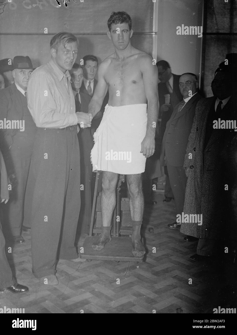 Marie Strickland and Walter Neusel weigh in for Wembley fight. Marie Strickland and Walter Neusel, the German, weighed in at the British Board of Boxing Control Offices at Dean Street, Soho, for their heavyweight fight tonight (Tuesday) at the Wembley Arena. Photo shows, Maurice Strickland (on scales), shaking hands Walter Neusel at the weigh in. 19 October 1937 Stock Photo