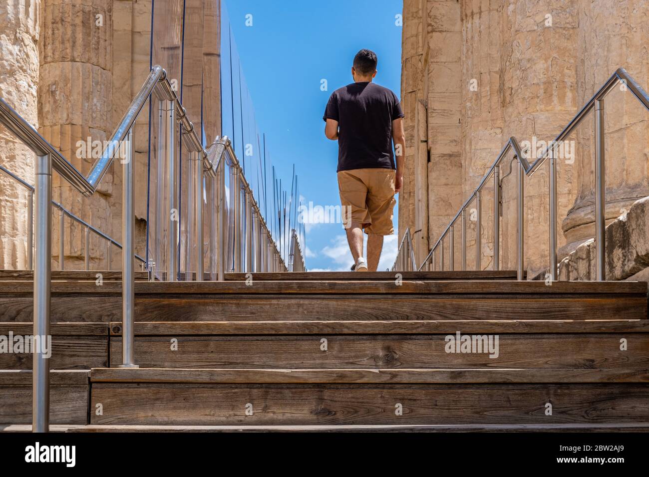 Athens Acropolis, Greece landmark. Young man back view walking alone on wood deck and stairs, Ancient Greek Propylaea, protective partitions measures Stock Photo