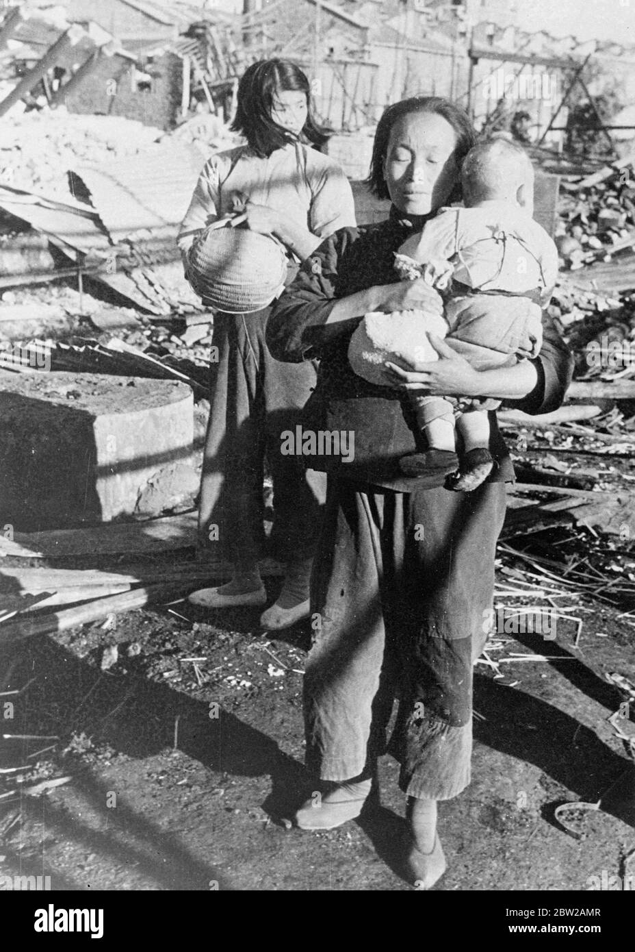 Japanese feed starving Chinese refugees in Shanghai. These pictures, just received in London, or made as hundreds of Chinese refugees from Shanghai, most of them starving and in a pitiful condition, received a ration of rise from the Japanese at Yangtzepoo, Shanghai. Large numbers of women and children were among those who flocked with baskets around the Japanese soldiers, who, on this occasion, represented the only hope of keeping alive. Photo shows, a mother, nursing a tiny baby, holds a bundle containing a ration of rice at Yangztzepoo. 2 November 1937 Stock Photo