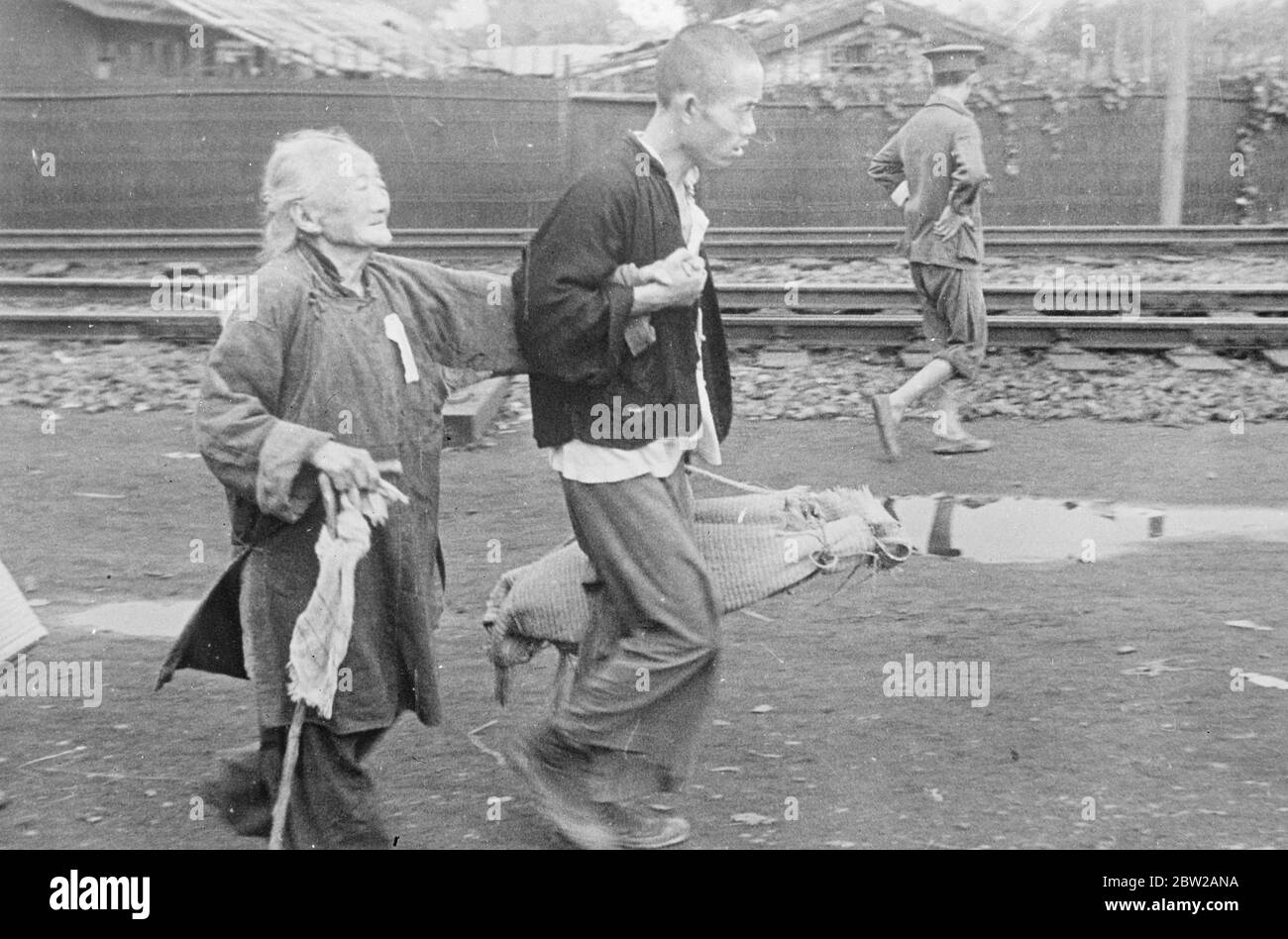 War has no pity for the aged!. An aged Chinese woman, one feeble hand grasping her stick, desperately endeavours to keep her flagging body abreast with her companion as they fly from the Shanghai. The man carries the old woman's few possessions in a small bundle. 21 November 1937 Stock Photo
