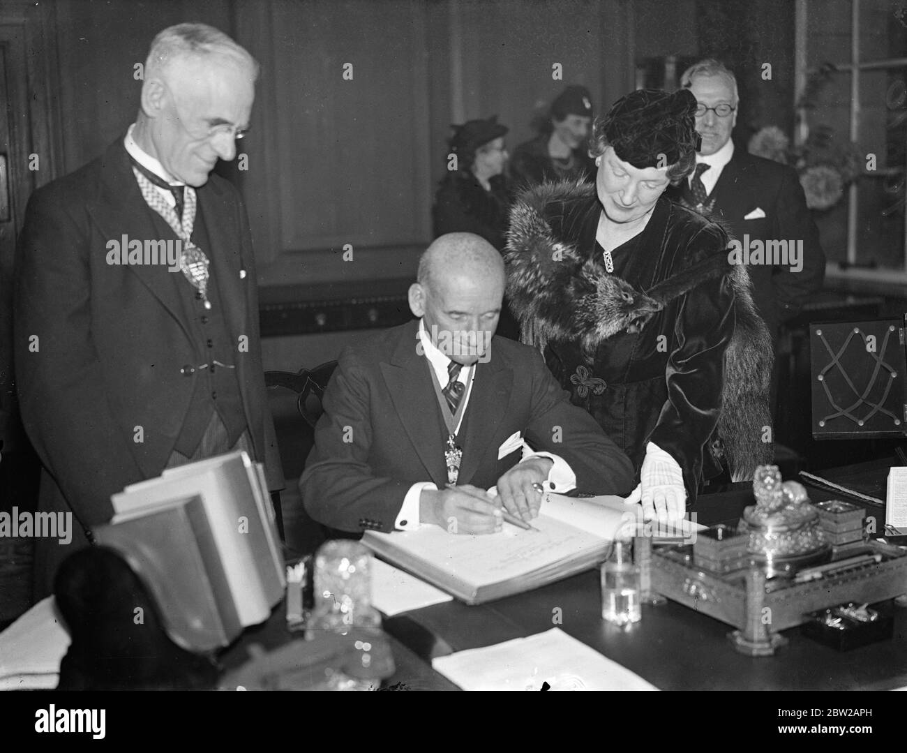 Lord Mayor and lady Mayoress at County Hall. The Lord Mayor of London, Sir George Broadbridge, and the lady Mayoress, attended a meeting of the London County Council at County Hall, Westminster. Photo shows, the Lord Mayor of London, signing the distinguished visitors book. Watched by the lady Mayoress and Lord Snell, chairman of the London county council. 2 November1937 Stock Photo