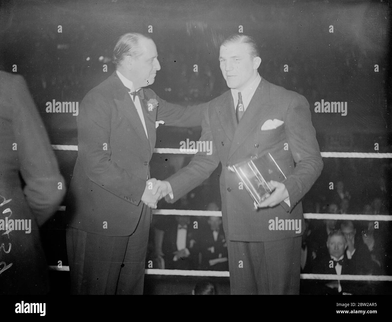 Tommy Farr receives NSC trophy at Wembley. Tommy Farr, British Empire heavyweight champion, attended the fight between Walter Neusel, the German and Maurice Strickland of New Zealand, at the Wembley Arena, London, and received the National Sporting Club Trophy from Sir Noel Curtis Bennett. The trophy was presented for as gallant showing against Joe Louis for the world title. Photo shows, Tommy Farr shaking hands with Sir Noel Curtis Bennett after receiving the trophy at Wembley. 19 October 1937 Stock Photo