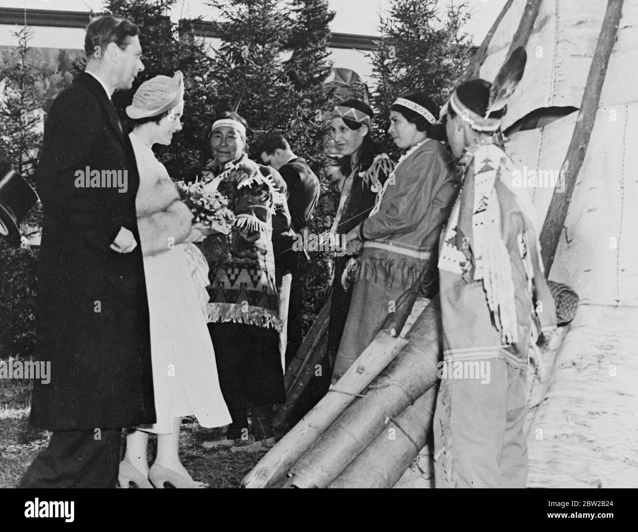 Original caption: The Royal Visit to Canada. The King and Queen visited the Ojibway Indians [Ojibwe / Ojibwa / Chippewa / First Nations] at the settlement which they made on the banks of the McIntyre River in the Port Arthur district of Ontario. Photo shows the King and Queen chatting to Indians who for the occasion discarded their modern clothes and wore tribal costumes and feathers. [Port Arthur, Fort William, Neebing formed the city of Thunder Bay in 1970s] 31 May 1939 Stock Photo