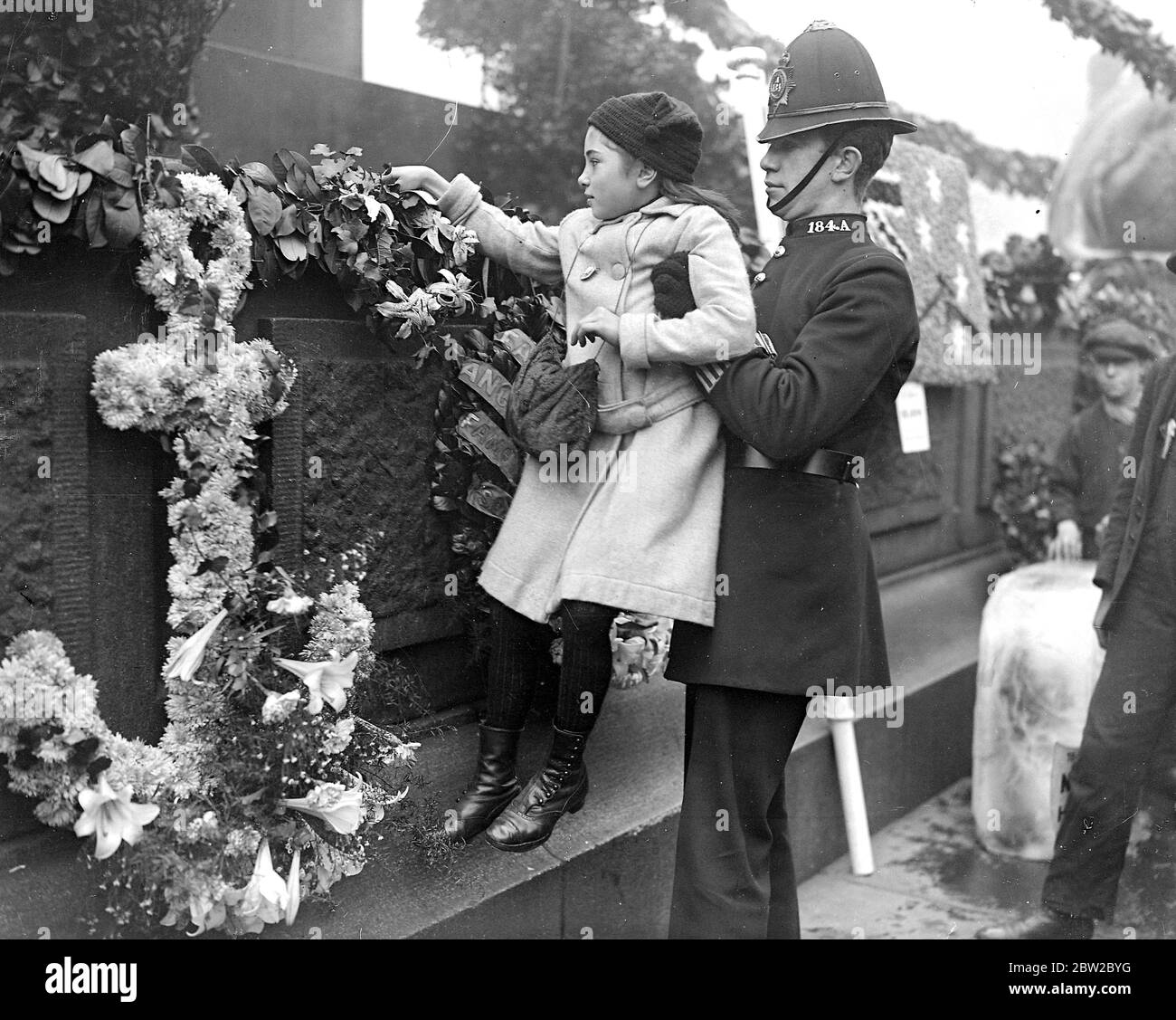 Trafalgar Day 1916. A kindly policeman lifts a little girl that she may deposit a wreath in memory of a near relative lost in a submarine. 21st October 1916 Stock Photo