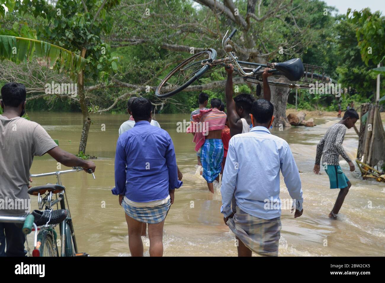 Local people wading water to cross the submerged road due to constant