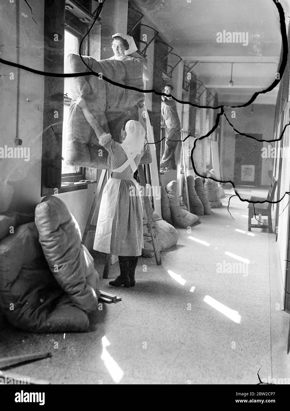 Precautions which will enable the essential work of the hospital to continue despite the danger of air raids in wartime are being taken at the Middlesex Hospital, London. Nurses use mattresses to block up windows. 29 August 1939 Stock Photo