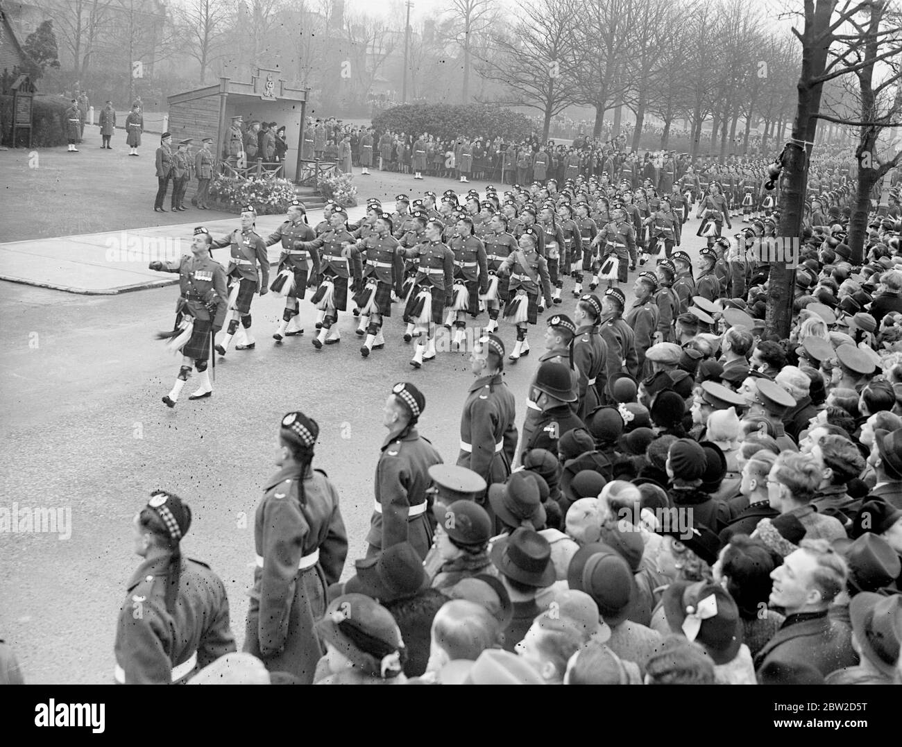 The King George VI and Queen Elizabeth, who have just returned from Sandringham, attended the dedication of the new West Wing of the St Andrews Garrison Church of Scotland at Aldershot Camp, Hampshire, and afterwards inspected the Scots regiments. Photo shows: The King and Queen at the saluting base as Scots troops march past 5 February 1939 Stock Photo