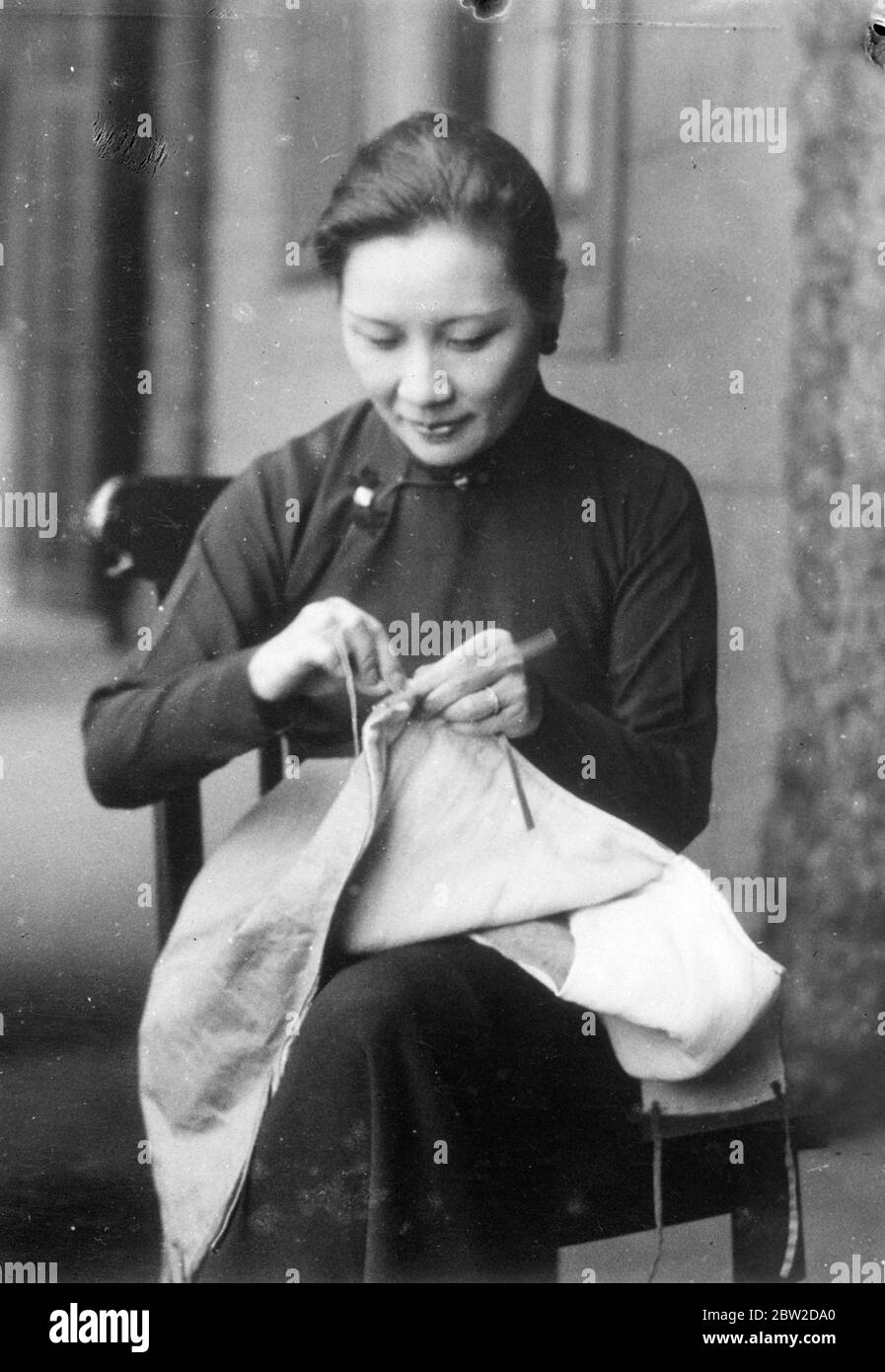 Madame Chiang Kai-shek, wife of the Chinese Generalissimo and First Lady of China, has been taking time off from affairs of state, in which she is one of her husband's most trusted advisers, to sew clothing for soldiers and refugees under the auspices of the New Life Women's Working Groups, which have their headquarters in the Yokohama Special Bank building in Hankow, the provisional Chinese headquarters. Photo shows: Madame Chiang sewing a soldiers padded vest. Stock Photo