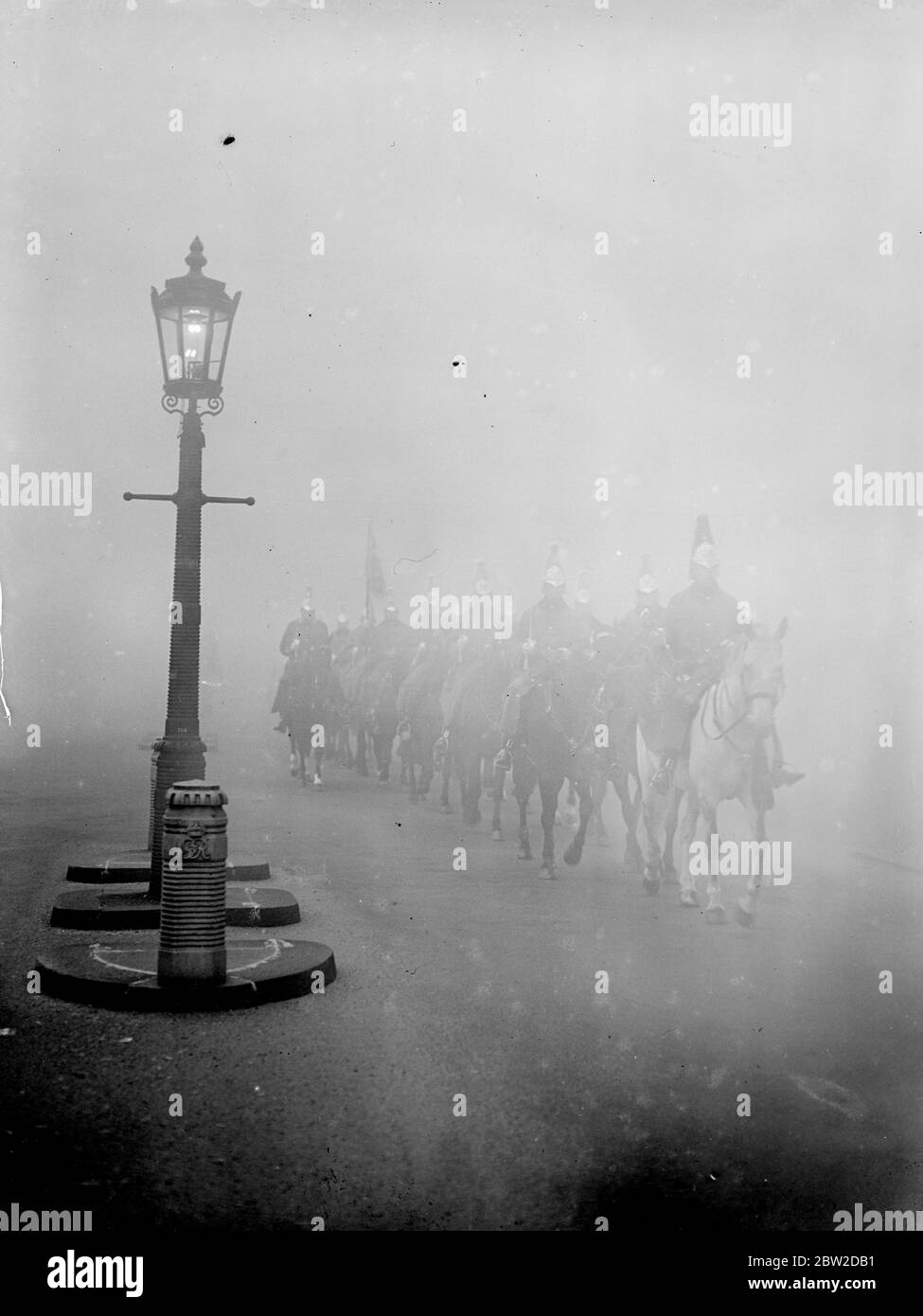 A lighted lamppost illuminate the way for horseguards as the pass through Hyde Park in the fog to take their turn of duty on the Horse Guards Parade. 24 October 1938 Stock Photo
