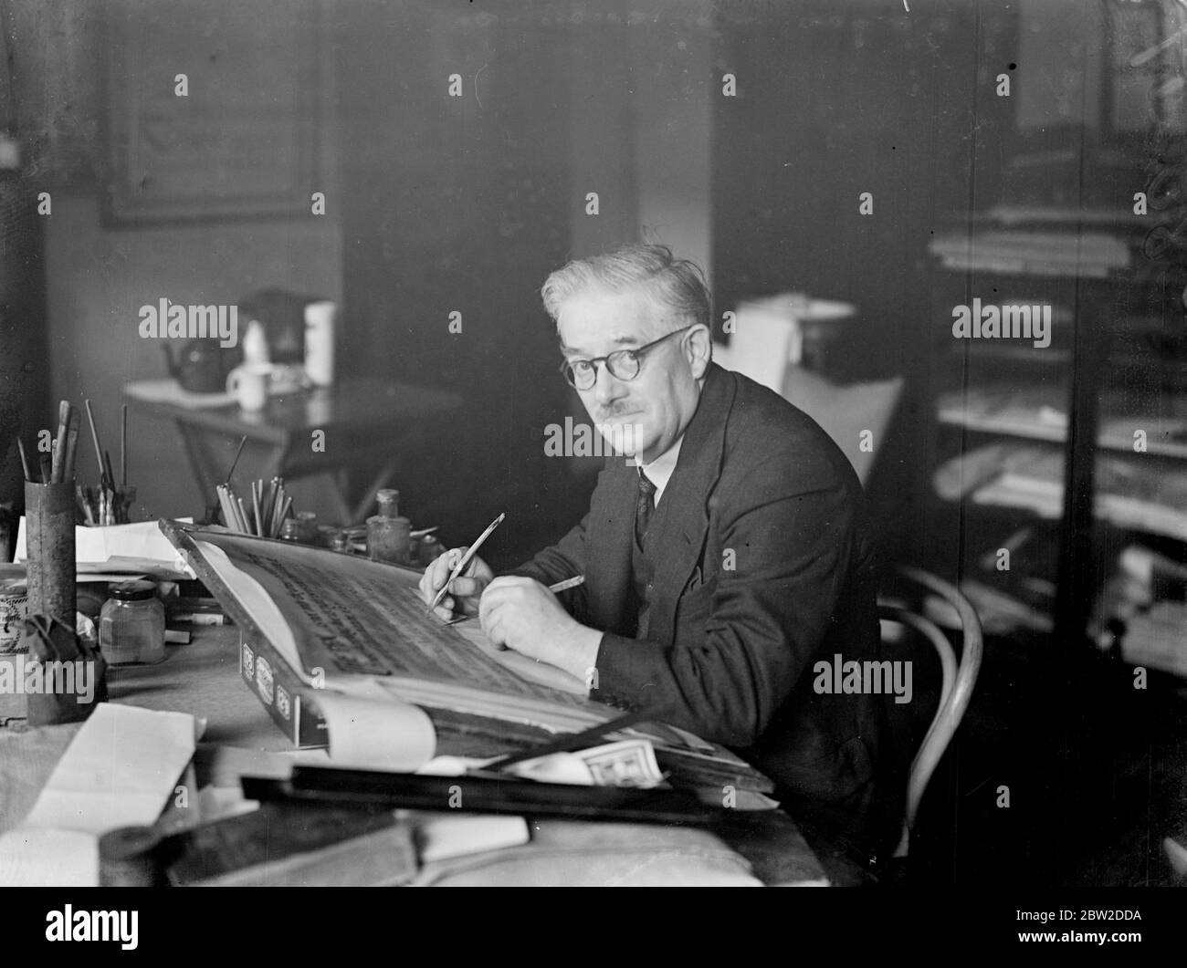 When the city of London presenters its Freedom to the Premier, Mr Neville Chamberlain, in recognition of his bid for world peace at Munich, the beautiful illuminated Scroll with will bear the beautiful handwork of Mr Henry James Mainwaring of London. Mr Mainwaring has been commissioned to write the scroll. Photo shows: Mr Henry James Mainwaring at work on a scroll in his London studio. 21 October 1938 Stock Photo