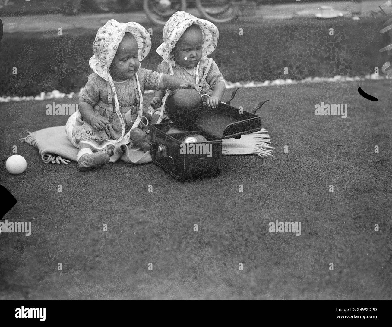 Jacqueline (left) getting ready to hand another bowl to Mrs Hallet as Jill watches her mother in play. The ten months old twins accompanied their mother when she competed in the singles events of the women's National Bowls Championships at Wimbledon Park, London. 26 August 1937 Stock Photo