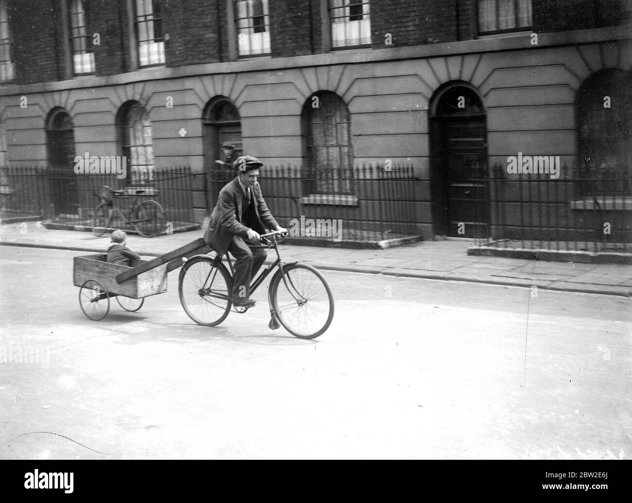 Man riding a bike with a small child in a boxcart. 1933 Stock Photo