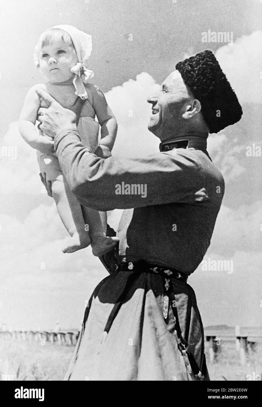 A smiling cossack lutenist, far removed from the wild ruthless horsemen visualised by most people outside Russia lifts up his chubby little daughter to show her the camp which he is stationed in the North. 16 August 1937. Stock Photo