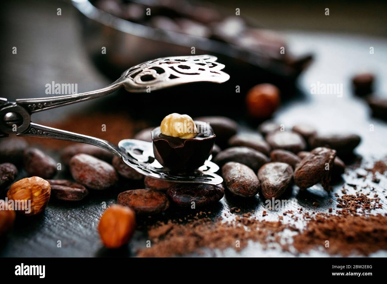 Chocolate candy with hazelnut on top stand on open dessert tongs beside bulk measuring scoop