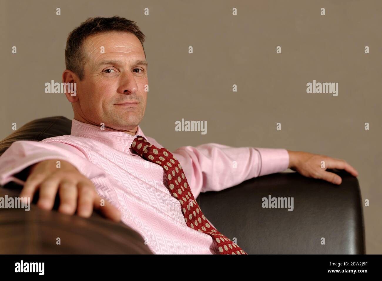 A businessman sitting confidently on a brown leather sofa Stock Photo