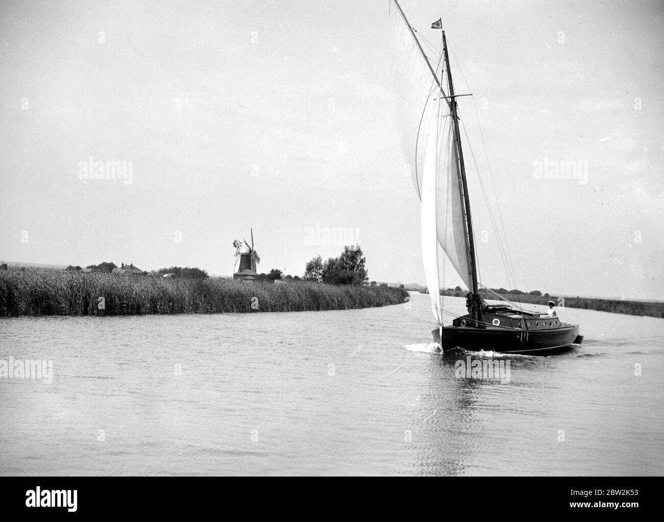 The Broads, Norfolk. Wherry sailing on a river / canal, a windmill in the background 1934 Stock Photo