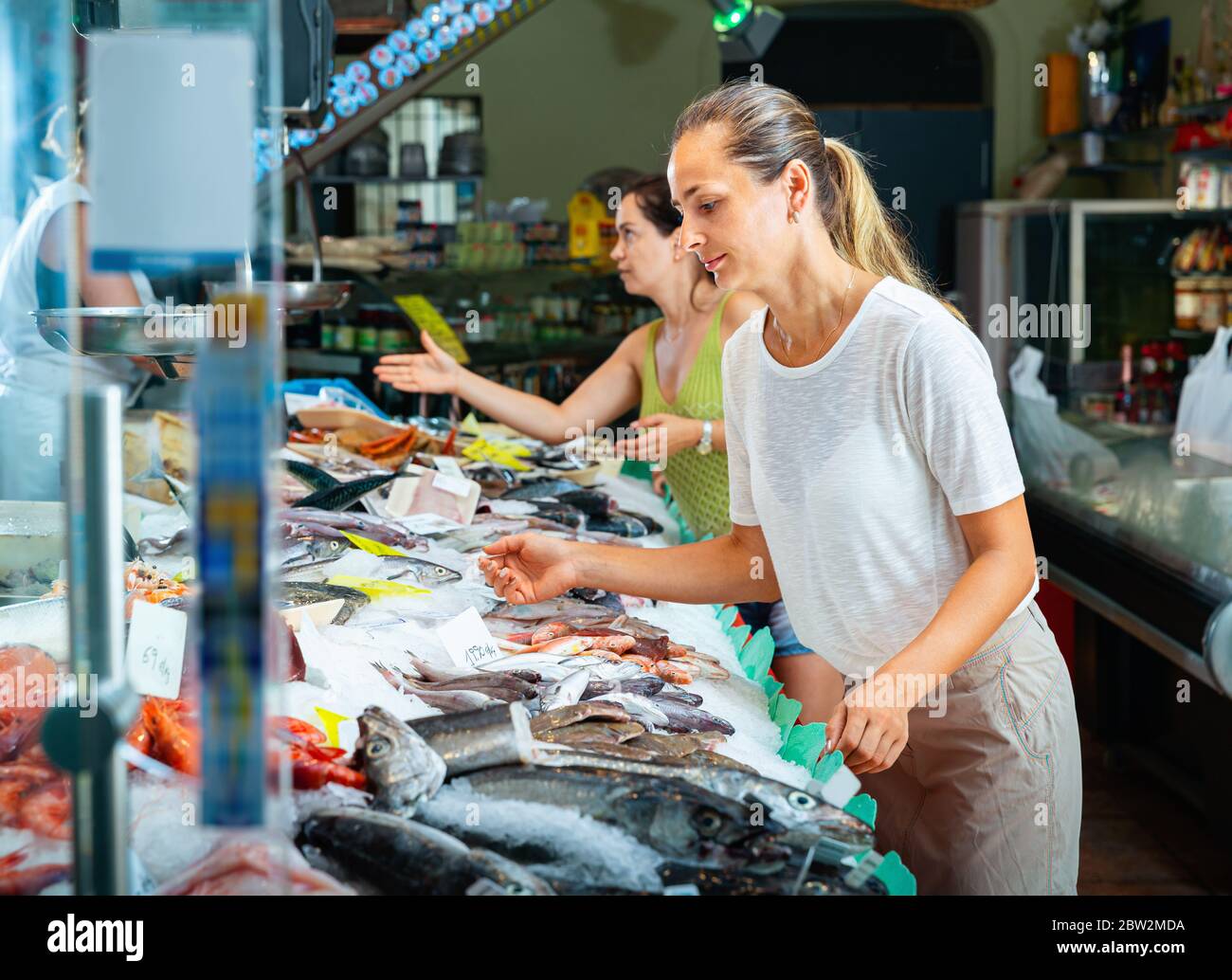 Cheerful positive women looking for fresh marine products on icy showcase of seafood market Stock Photo