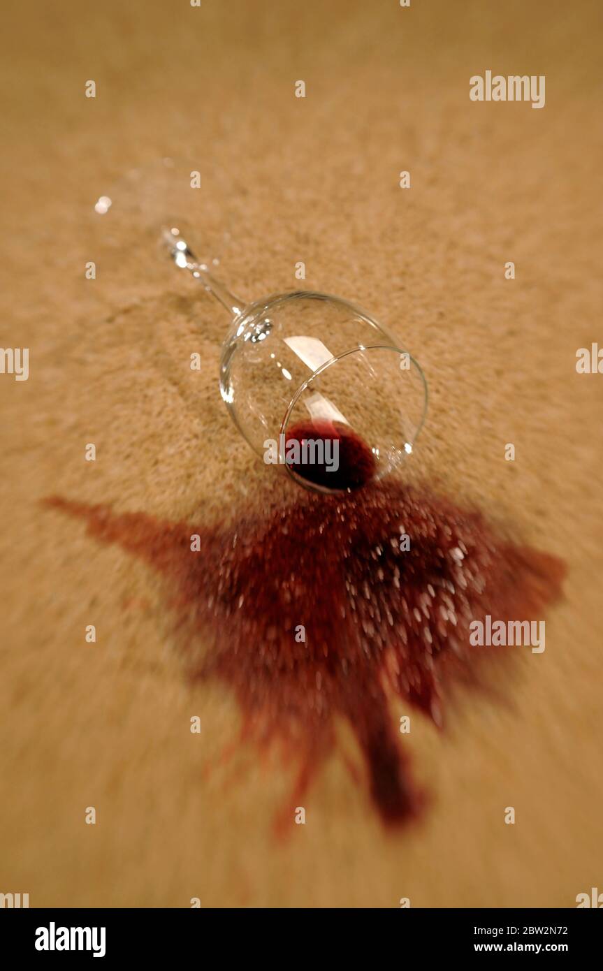 A glass of red wine spilling on a carpet Stock Photo