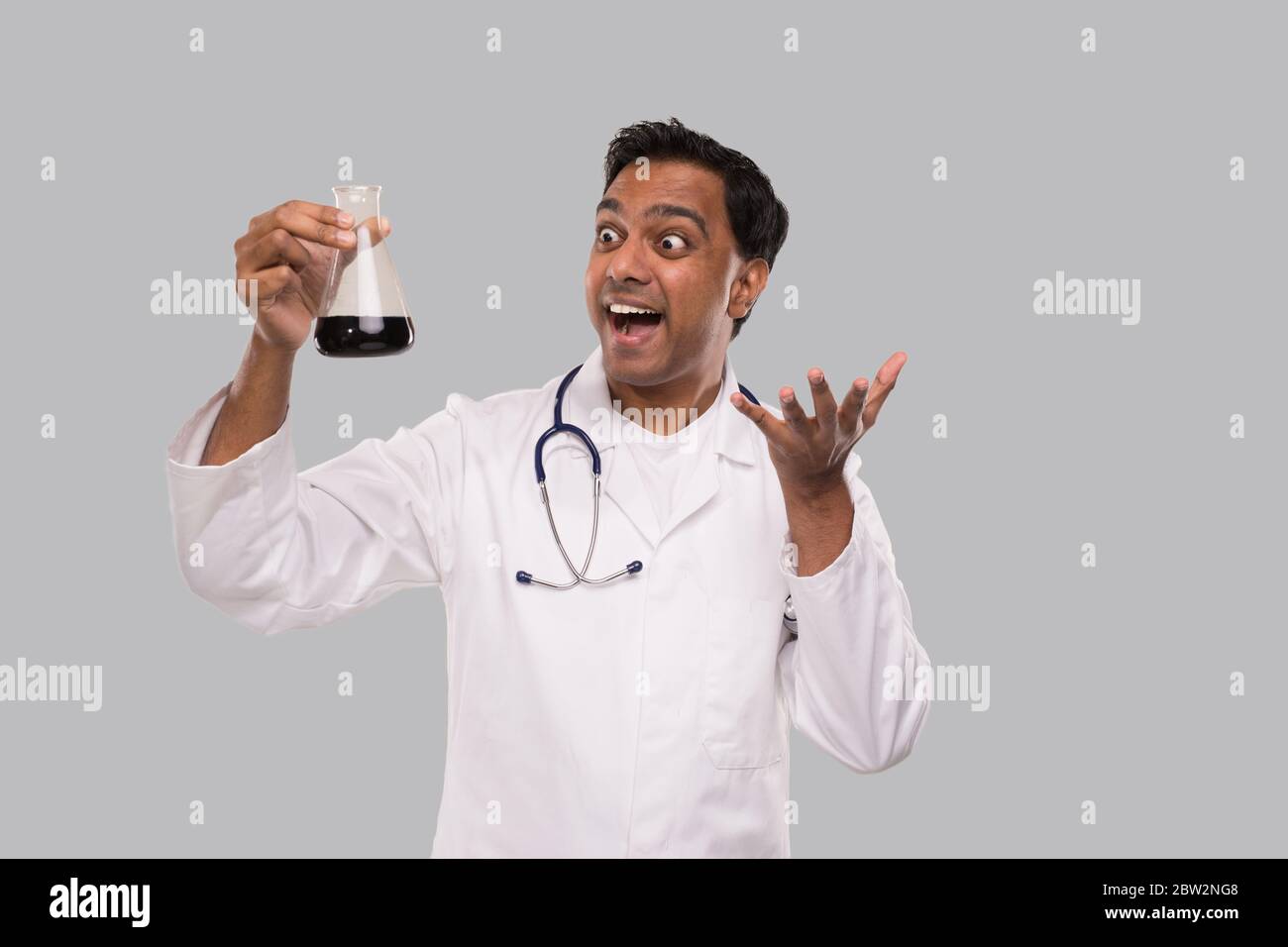 Male Doctor Excited Watching Flask with Colorfull Liquid Isolated. Science, Medical, Virus Concept. Indian Man Doctor Smilling. Stock Photo