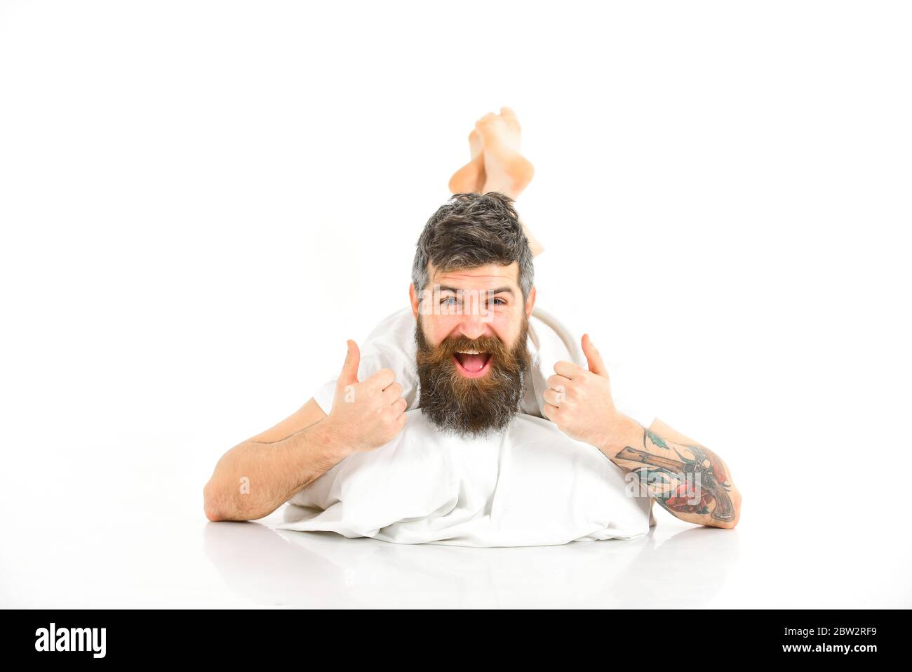 Hipster with beard shows thumbs up gesture, energetic and successful macho.  Man full of energy in morning, white background. Energetic man concept. Man  with happy face lies on belly Stock Photo -, image size:1300x957